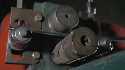 Forge workshop on table. Worker bends the metal rod on the wrought iron round bending machine. Manufacturing of a designer part from a metal rod.