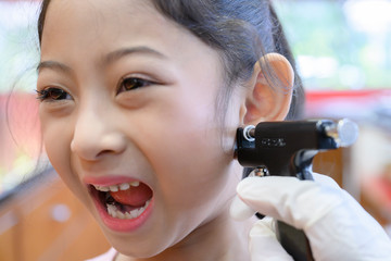 Adorable little Asian girl having ear piercing process. - 295228308