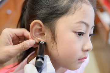Adorable little Asian girl having ear piercing process. - 295228337