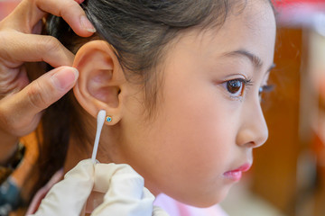 Adorable little Asian girl having ear piercing process. - 295228363