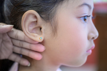Adorable little Asian girl having ear piercing process. - 295228385