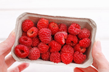 Woman hold paper box with raspberries.