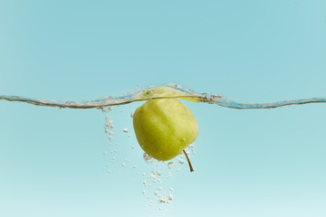 ripe green apple in water with bubbles on blue background