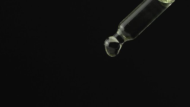 Oil or liquid dropper or pipette in extreme macro close up. Drop of yellow cosmetic lavender oil falling on black background. Eyedropper squeezing out meds droplets.