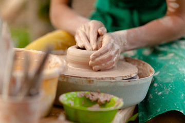Hand craft making pottery on wheel. Female hands mold ceramic plate from clay (pot).