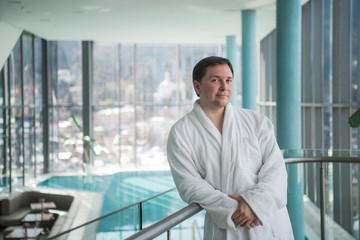Fototapeta premium Adult man in a bathrobe standing in the spa in front of a pool