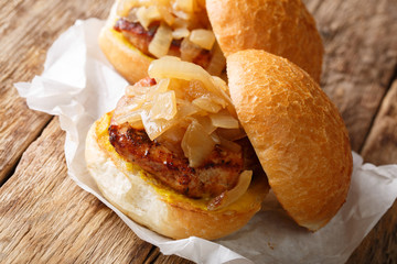 Pan fried onions and pork chops served on hamburger buns close-up on paper. horizontal