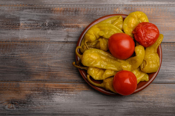 Assorted pickled peppers and tomatoes on a ceramic plate on a wooden background