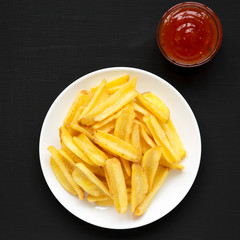 Homemade french fries with sour-sweet sauce on a white plate on a black background, top view. Flat lay, overhead, from above.