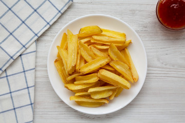 Homemade french fries with sour-sweet sauce on a white plate on a white wooden table, top view. Flat lay, overhead, from above. Close-up.