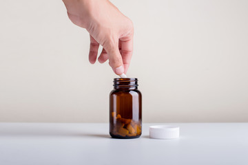 The hand that is picking the supplement out of the bottle on a white background.Dietary supplement...