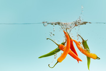 colorful chili peppers falling deep in water with splash on blue background