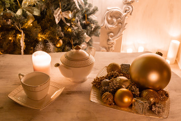 Tea time, white teapot and cups on the table. Decorated Christmas tree. Classic apartments with a white fireplace.