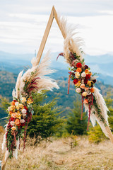 Triangular wooden arch with composition of pampasian grass, dahlia and roses. Decorative floristry