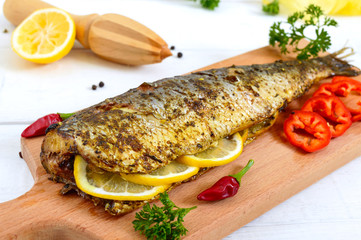 Baked herring with lemon and spices on a white wooden background. Tasty fish dish.