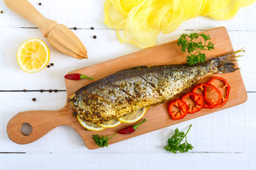 Baked herring with lemon and spices on a white wooden background. Tasty fish dish. Top view.