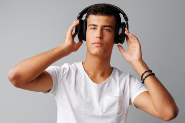 Young man teenager listening to music with his headphones over a grey background