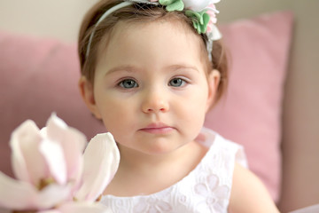 beautiful baby girl in a white dress holds a magnolia in her hand