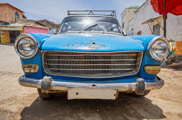 Front part side of an old blue 60's car very used on a dirt road.