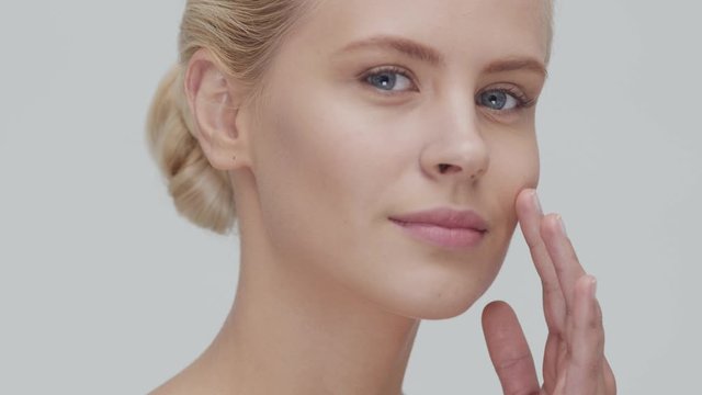 Studio portrait of young, beautiful and natural blond woman applying skin care cream. Face lifting, cosmetics and make-up.