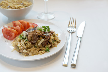 low carb risotto made from cauliflower with porcini mushrooms, parsley, parmesan and tomatoes on a plate, white table, copy space