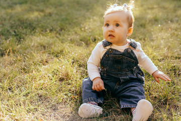 Portrait of a little baby girl seating and playing on green grass of park. - Image
