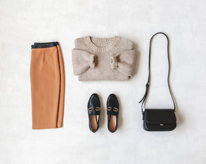 Brown midi pensil skirt, beige knitted oversize sweater, cross body bag, black loafers or flat shoes on grey background. Overhead view of women's casual day outfit. Flat lay, top view. Women clothes.