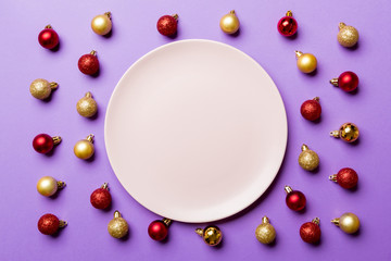 Top view of festive plate with red and golden baubles on colorful background. Christmas decorations and toys. New Year advent concept