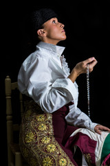 Woman Bullfighter in Chapel praying with Rosary on her hand on a black background
