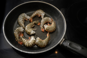 roasting raw black tiger prawn shrimps with shell but without head in a pan on the stove, cooking a tasty meal for low carb diet