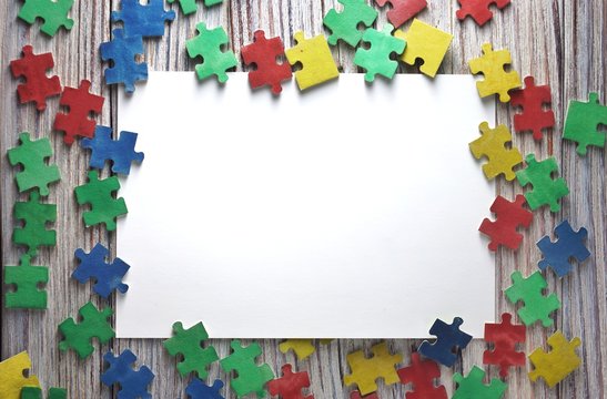 colorful puzzles on white wooden background with white paper sheets, frame, early childhood autism concept, mocap, copy space, text space.