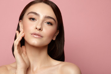 young girl with hand near face with clean skin, natural makeup and white teeth on a pink background