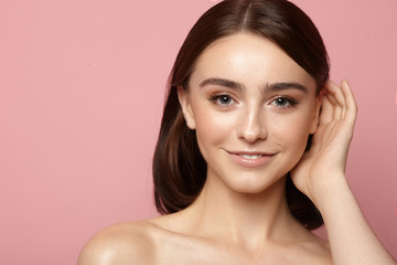 young girl combing her hair with clean skin, natural makeup and white teeth on a pink background