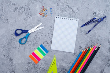 colored pencils, stickers, notepad, paper clips, scissors, ruler and compasses lie on a gray background, space for text. Top view, flat lay. template. office supplies
