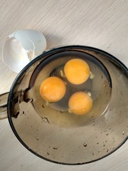 Three raw eggs in a dark glass mug close up