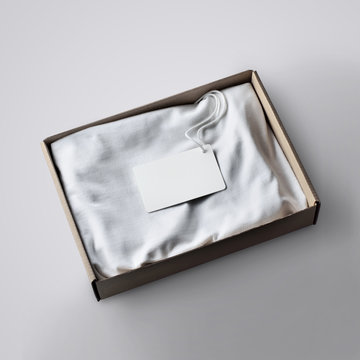 Folded  blank T-shirt with white label  in the cartoon box on the studio background.