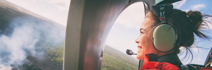 Helicopter doors off ride adventure travel Asian woman tourist happy looking at landscape of volcanic eruption above volcano fumes in Big Island, Hawaii. Panoramic banner background.