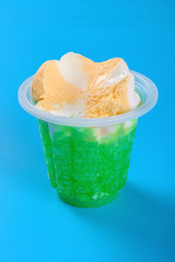 side view cup of orange and green color ice cream with some bites on blue background