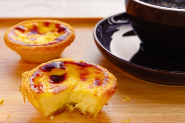 fresh portuguese egg tarts with a quarter cut out and cup of coffee on back