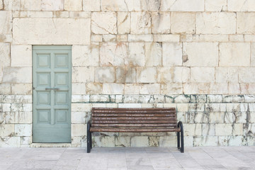 un banc en bois devant un mur de pierre et une porte bleue en Italie - obrazy, fototapety, plakaty