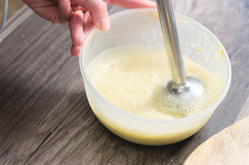 close-up whipping the mixture of homemade mayonnaise with a blender in a plastic bowl