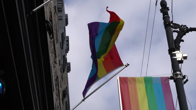 The pride flag is moving fast with a strong wind effect. The flag is in front of a store.