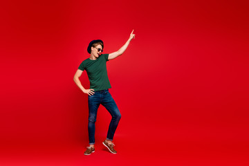 Full size profile side photo of crazy guy have fun on summer weekends celebration aprty dance raise index finger wear denim jeans sneakers outfit isolated over red color background