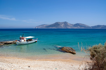 Greece - the island of Koufonissi.  A white painted small fishing boat, docked at a little concrete quay. In the distance is the island of Keros.   A summers day with crystal clear blue sea water.