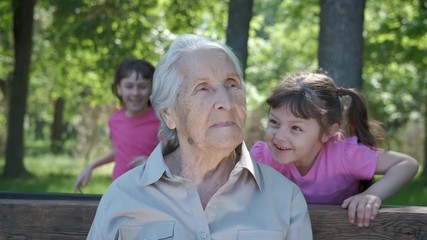 Grandchildren hug grandmother. Happy little girls hug grandmother in a summer park.