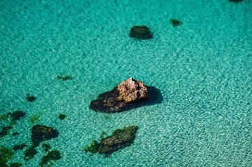 tourists are resting on the rocks and swimming in the sea.