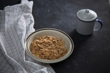 Wheat bran breakfast cereal with no milk in a bowl. Black background with homespun napkin.
