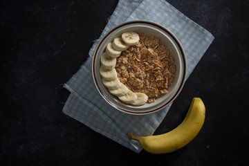 Organic healthy oatmeal porridge with fresh bananas. The white porcelain bowl with napkin underneath bowl.