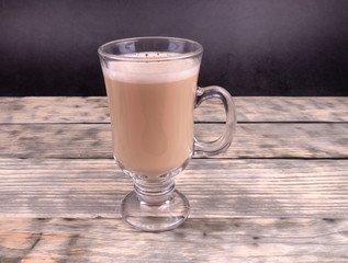 One glass cup of hot coffee with milk standing on wooden background