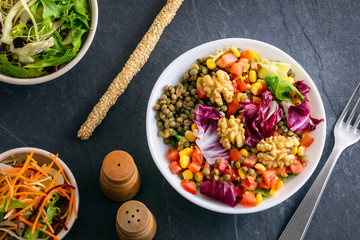 Healthy autumn salad bowl lunch with nuts, green lentils, corn, tomato,  lettuce, spinach with sesame seeds